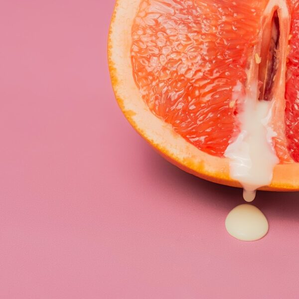 High angle of closeup of half of fresh orange grapefruit as symbol of vagina with sperm placed on pink surface in studio